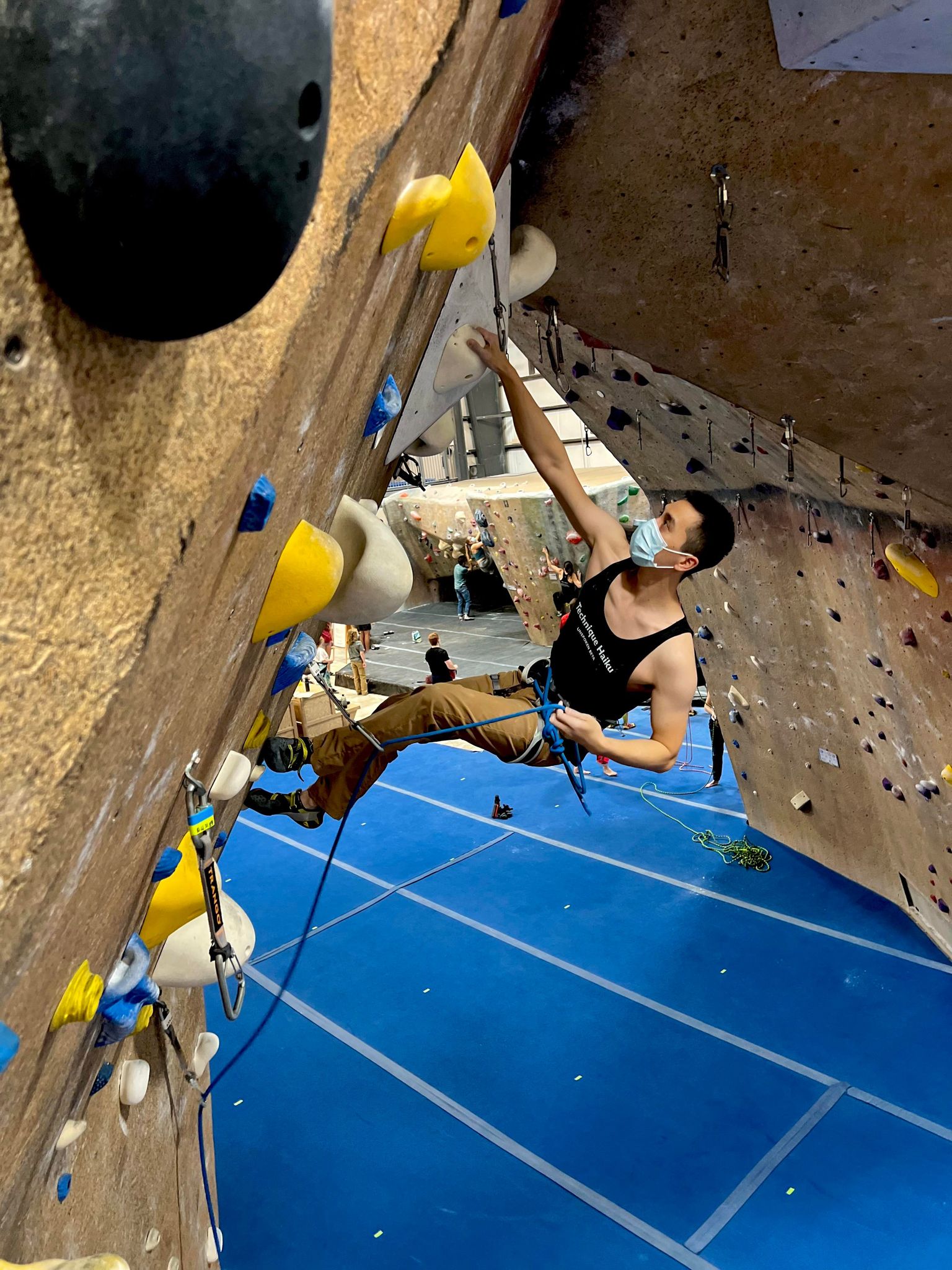 Charcoal black tank top shirt with "Technique Haiku, Unspoken Beta" on the front worn by male lead climbing on a climbing wall in the gym