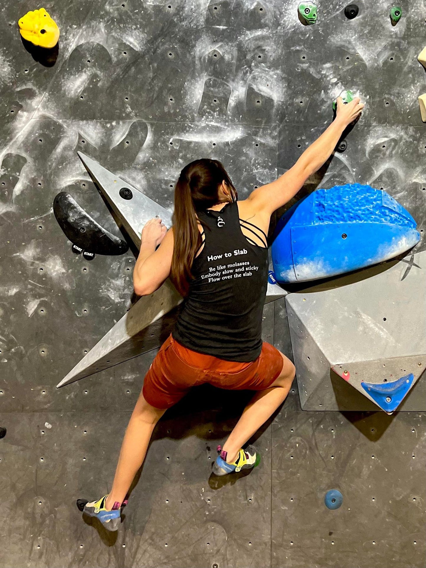 Charcoal black tank top shirt with How to Slab haiku on the back worn by female bouldering on a climbing wall in the gym