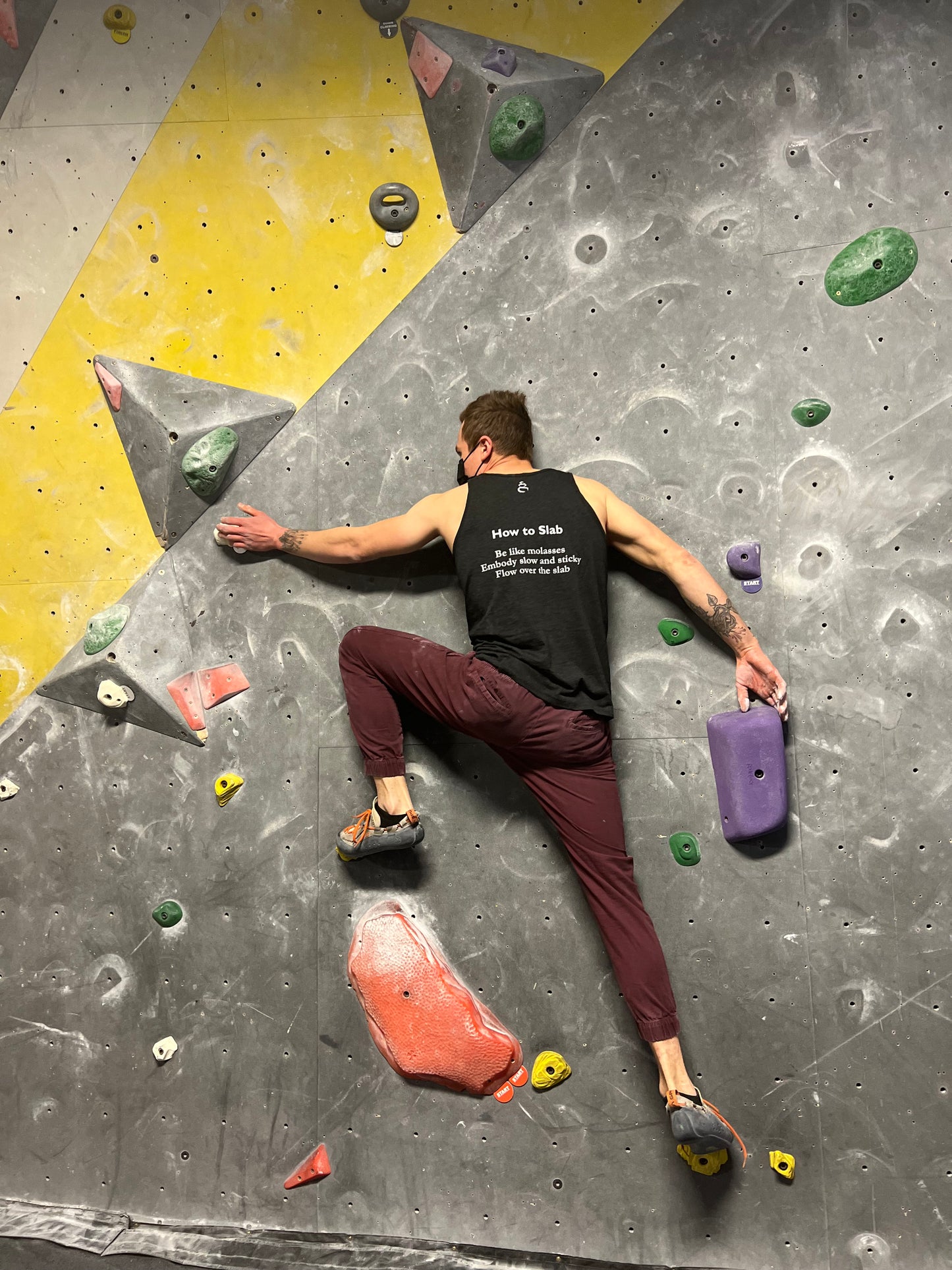 Charcoal black tank top shirt with How to Slab haiku on the back worn by male bouldering on a climbing wall in the gym
